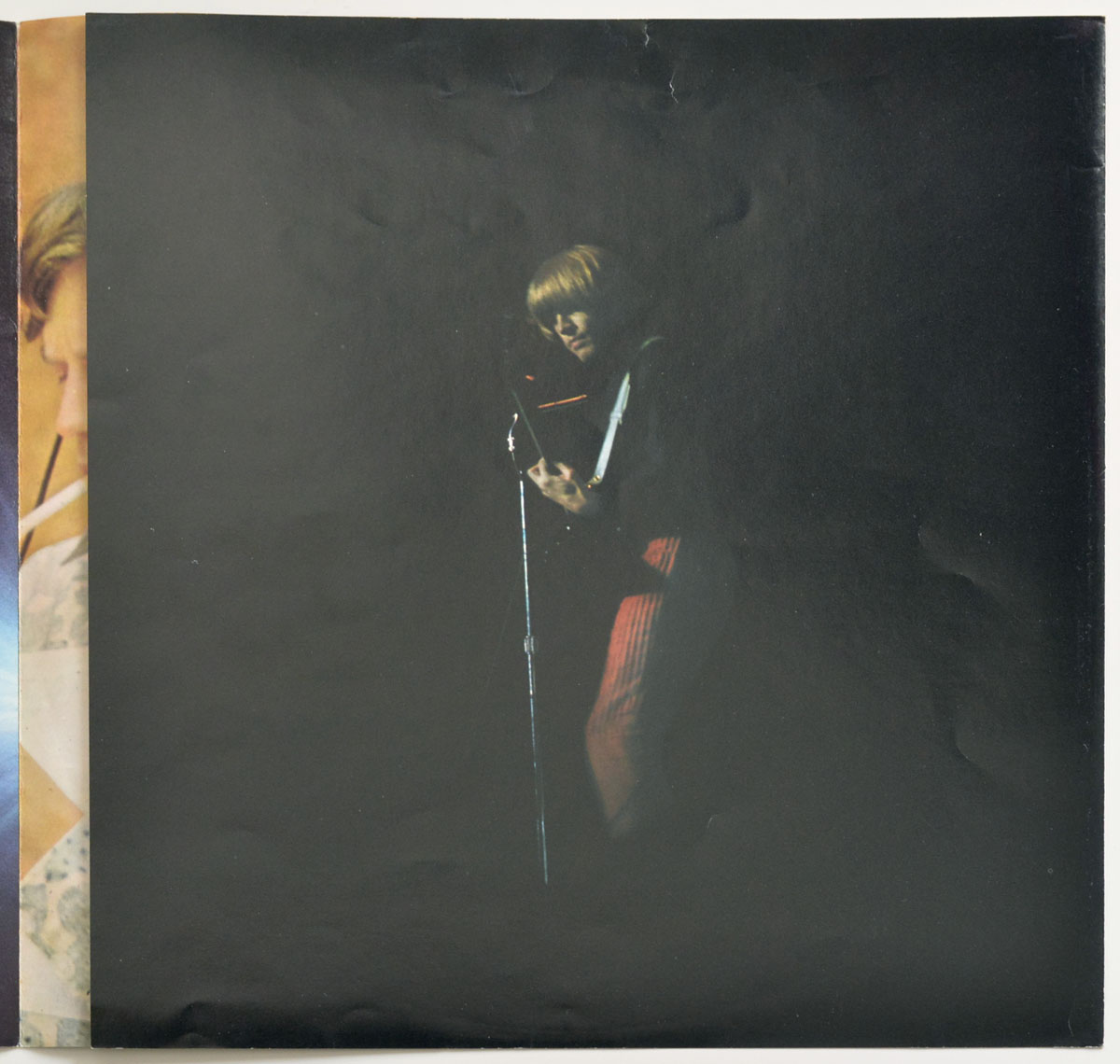 Dramatic low-light photo of Brian Jones performing live, illuminated in a beam of light against a dark stage backdrop, from the 1974 German Rolling Stones Big Hits booklet.